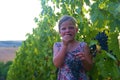 Cute girl little six years old girl eating a fresh blue grape directly from the plant in a red vineyard. Concept of Royalty Free Stock Photo