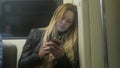 Cute girl with long blonde hair in leather jacket straightens use gadget in metro