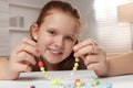 Cute girl making beaded jewelry at table in room Royalty Free Stock Photo