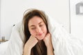 Cute girl with messy hair, lying in bed covered in white sheets duvet, smiling and laughing coquettish, spending time in Royalty Free Stock Photo