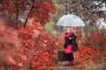 Cute girl with an old suitcase and an umbrella in her hand on a footpath in the autumn forest Royalty Free Stock Photo