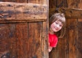 Cute girl peeping behind an old wooden door Royalty Free Stock Photo