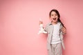 A cute girl in a pigtail holds the ears of a plush hare with her hand and opens her mouth in surprise Royalty Free Stock Photo