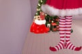 Cute girl with pointed elven feet wearing elf legging standing in a room with a christmas tree and santa claus bag full of