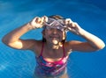 Cute young well-tanned girl in the pool takes off or puts on her diving mask.