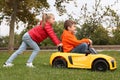 Cute girl pushing children`s car with little boy in park