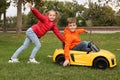 Cute girl pushing children`s car with little boy in park
