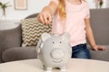 Cute girl putting coin into piggy bank at table. Saving money Royalty Free Stock Photo