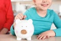 Cute girl putting coin into piggy bank at table. Saving money Royalty Free Stock Photo