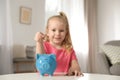 Cute girl putting coin into piggy bank at table. Saving money Royalty Free Stock Photo