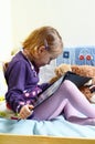 Cute girl reading a book on her bed with toys around her Royalty Free Stock Photo