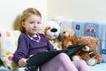 Cute girl reading a book on her bed with toys around her Royalty Free Stock Photo