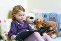 Cute girl reading a book on her bed with toys around her Royalty Free Stock Photo