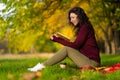 A cute girl reads a book and drinks coffee on a green lawn in an autumn park. Autumn mood. A cozy place to be alone with yourself Royalty Free Stock Photo