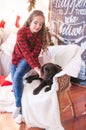 Cute girl in a red checkered shirt with dog labrador at home in the room decorated for Christmas. Royalty Free Stock Photo