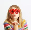 Cute girl with red heart-shaped glasses blowing ki