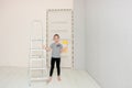 cute girl in the room where the renovation is underway stands next to the stepladder and holds a paint roller in her Royalty Free Stock Photo