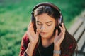 Cute girl`s face with headphones. Young woman enjoys music while sitting in green park. Concept of youth, freedom