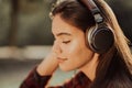 Cute girl`s face with headphones. Young woman enjoys music while sitting in green park. Concept of youth, freedom