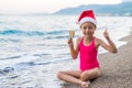 Cute girl in santa claus hat and lollipop on the beach, free space. Royalty Free Stock Photo