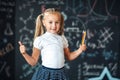 Cute girl in school uniform with colored pencils. Go to school for the first time. Girl indoors of the class room with blackboard