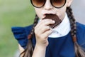 Cute girl, school years dressed in school uniform with pleasure eating black chocolate on the street in the park
