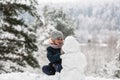 Cute girl sculpts snowman in winter day.