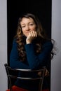 Cute girl sits on a bar chair and clouds her hands on the back of a chair, black gray background