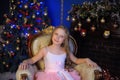 Cute girl sitting in a chair at the Christmas tree Royalty Free Stock Photo