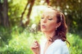 Cute girl sitting in a park and blowing on the dandelion. Natural look. Royalty Free Stock Photo