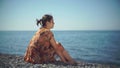 Cute girl sitting on the shore throwing pebbles into the sea