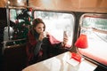 Cute girl sitting in the winter in a cozy cafe, drinking coffee and taking selfies against the background of the Christmas tree.