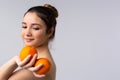 A cute girl smiles tenderly and holds two juicy oranges in her hand. Vitamins concept. Shine and skin care. Gray Royalty Free Stock Photo