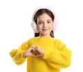 Cute girl in stylish earmuffs making heart with hands on white background