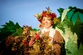 Cute girl in sweater, white scarf and green wings with bouquet of rowan branches with red berries and wreath in nature Royalty Free Stock Photo