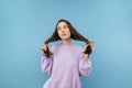 Cute girl in sweatshirt playing with hair and shy looking to the side, isolated on a blue background Royalty Free Stock Photo
