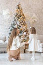 Cute girl toddler and her mom decorate the Christmas tree in the house. Happy family