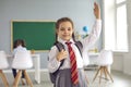 Cute girl in uniform raising hand, ready to answer her lesson at classroom. Portrait of adorable first grader at school Royalty Free Stock Photo