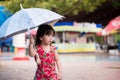 Cute girl walked in the middle of an umbrella to prevent the drizzle of rain. Adorable kid wearing a red dress.