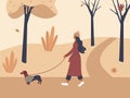 Cute girl walking with dog dachshund in overalls in autumn city park or forest. Fall soothing outdoors landscape: trees, leaves, Royalty Free Stock Photo