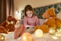 A cute girl wearing pyjamas sitting alone on a huge bed barefoot watching cartoons on a tablet before going to sleep Royalty Free Stock Photo