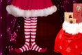 Cute girl wearing red white striped elf stockings and a cute dress standing next to a santa claus bag full of presents on a Royalty Free Stock Photo