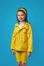 Cute girl wearing yellow raincoat with hood over blue wall, has good mood Royalty Free Stock Photo