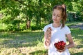 cute girl in white T-shirt is standing in garden and holding a glass vase with ripe cherries in her hands. Concept of gardening Royalty Free Stock Photo