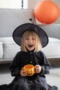 A cute girl in a witch hat is laughing at a Halloween party with a pumpkin-shaped mug in her hands. Happy Halloween Royalty Free Stock Photo