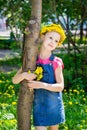 Cute girl in a wreath of dandelions holding a bouquet of dandelions in her hand stands embracing a tree trunk Royalty Free Stock Photo