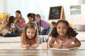 Cute girls drawing on floor while kindergarten teacher reading book to other children Royalty Free Stock Photo