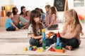 Cute girls playing with building blocks on floor while kindergarten teacher reading book to other children Royalty Free Stock Photo