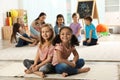 Cute girls sitting on floor while kindergarten teacher reading book to other children Royalty Free Stock Photo