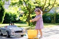 Cute gorgeous toddler girl washing big old toy car in summer garden, outdoors. Happy healthy little child cleaning car Royalty Free Stock Photo